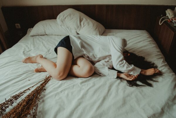 A woman experiencing constipation lying on a bed, covering her face